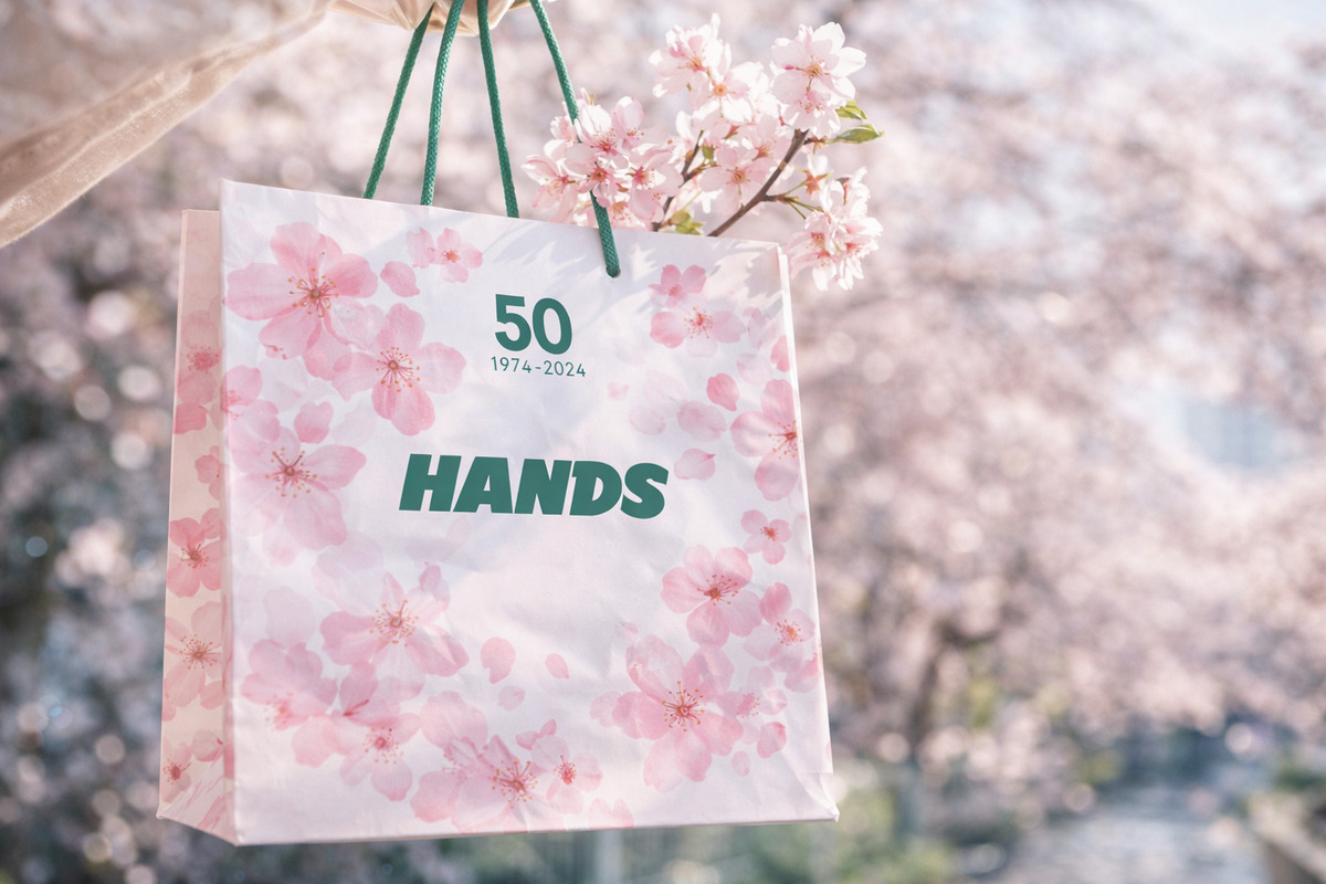 桜柄のショッパーと本物の桜が春の光に包まれ、季節の訪れを感じさせるやさしい雰囲気の一枚