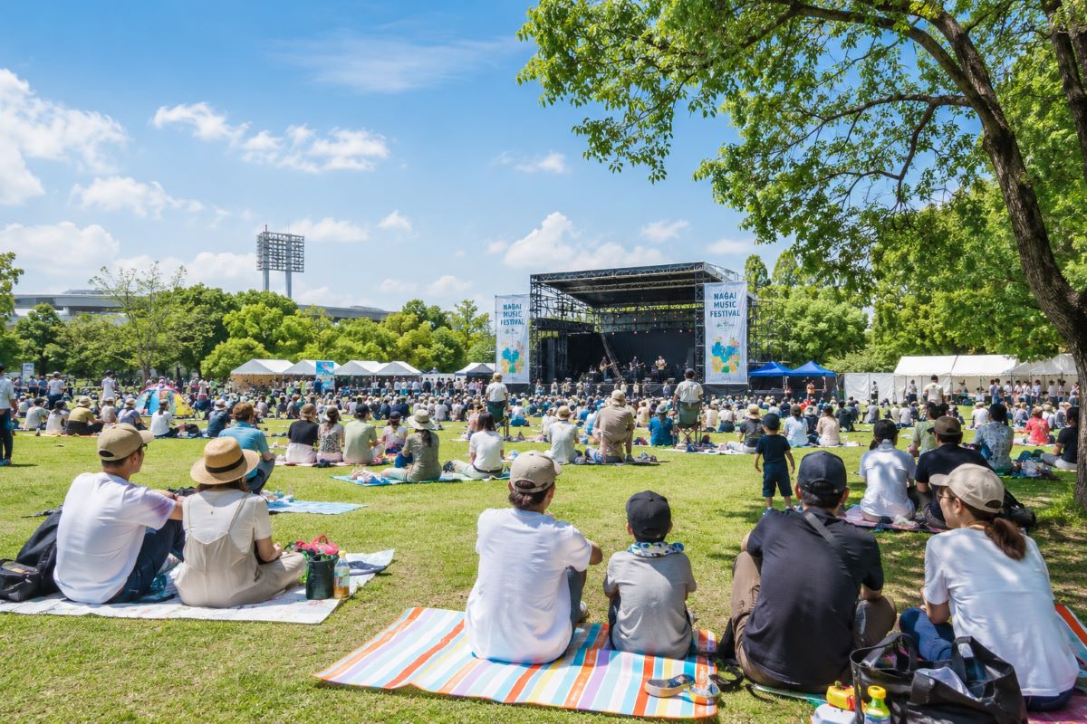 芝生広場に集まった来場者が青空の下で音楽を楽しむ長居音楽祭の風景