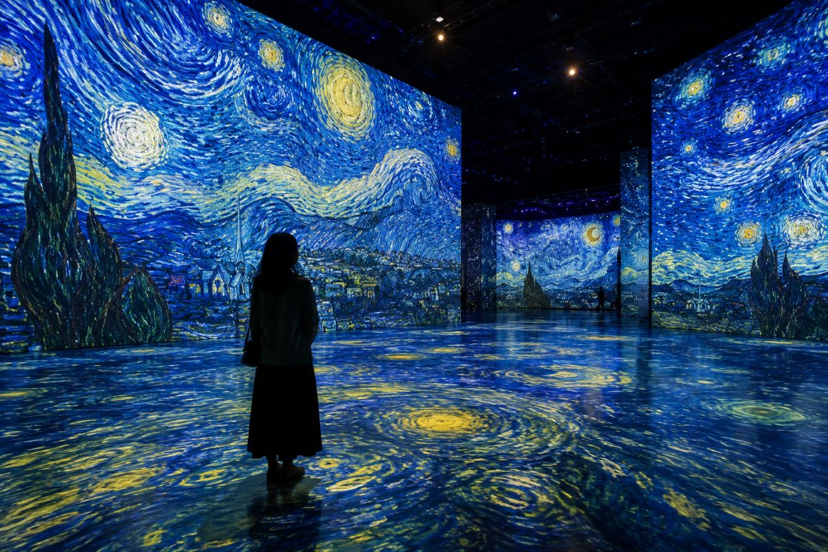 巨大な光の映像に包まれた没入型アート空間で、作品を見上げる来場者の姿