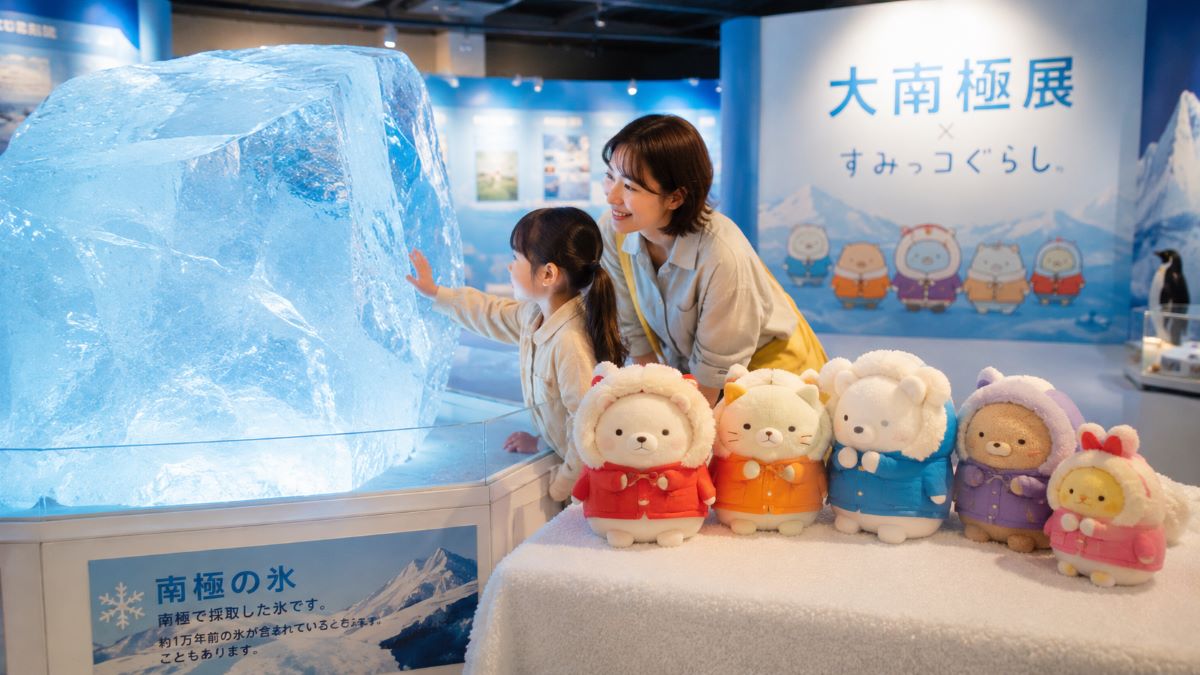 青く透き通る南極の氷に触れる子どもと見守る保護者、南極仕様のマスコットが並ぶ展示風景