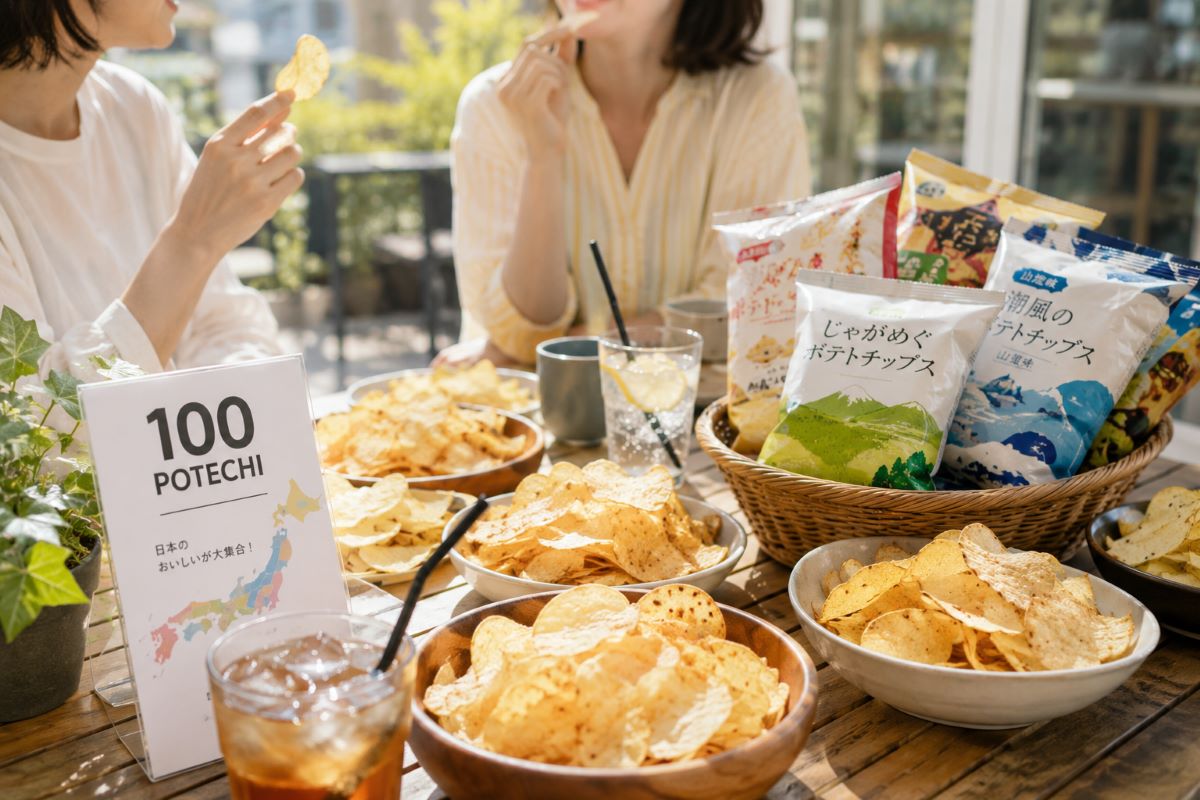 さまざまなご当地ポテトチップスが並ぶテーブルを囲みながら、初夏のテラスでおやつ時間を楽しむ人たちの様子
