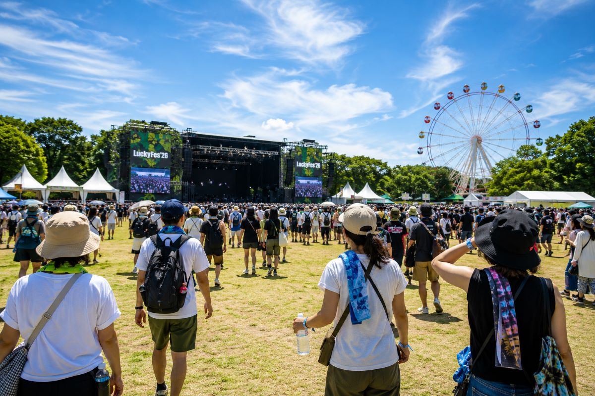 夏空の下、広い芝生会場を歩きながらフェス会場へ向かう来場者たちの様子