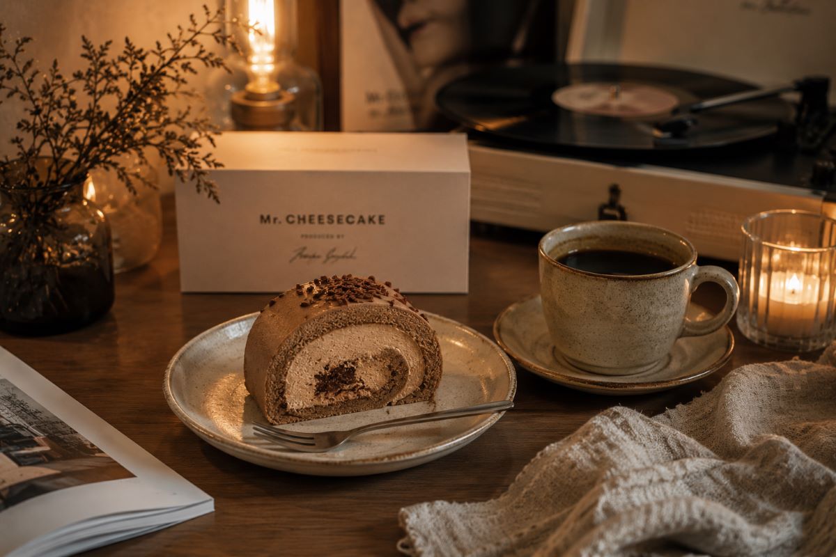 間接照明が灯る部屋でロールケーキとコーヒーを楽しみながら、ゆったりとしたおうちカフェ時間を過ごす様子