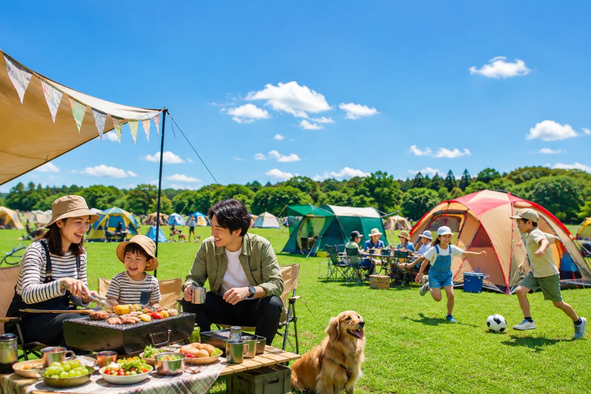青空の芝生広場でテントやBBQを楽しむ家族連れと犬が集うアウトドアイベントの風景